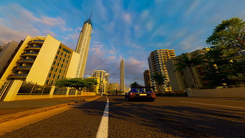 Cars on road by buildings against sky in city