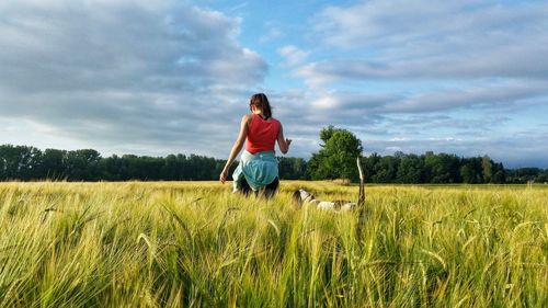 Rear view of woman with dog walking on wheat field against sky