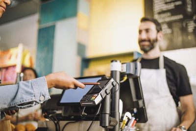 Cropped image of woman paying through smart phone at store checkout