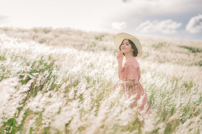 A young asian girl on a beautiful spring meadow. she wears a pink dress and wide-brimmed hat.