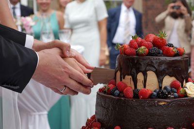 Cropped image of bride and groom cutting cake during wedding