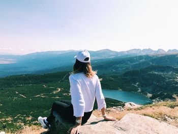 Woman sitting on mountain against sky