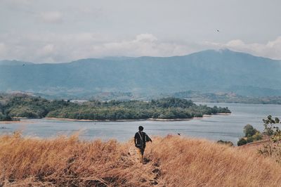 Rear view of man looking at lake against sky