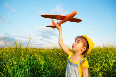 Portrait of young woman with arms raised standing on field against blue sky