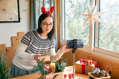 Female florist blogger making winter ikebana with pine branches, candle and christmas decorations