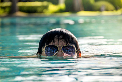 High section of person wearing sunglasses while swimming in lake
