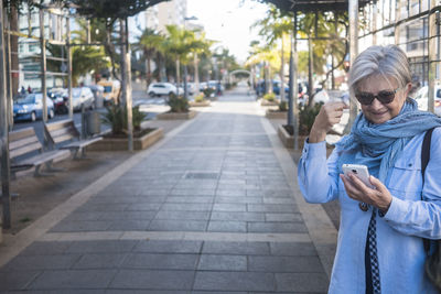 Senior woman using mobile phone standing on footpath