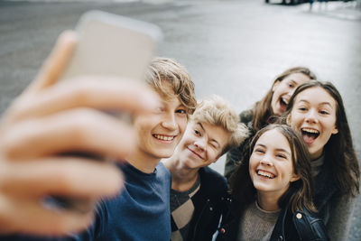 Smiling male taking selfie with friends through smart phone while standing in city