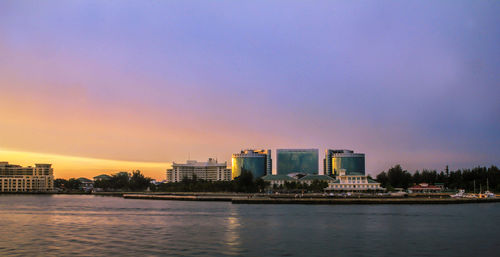 Buildings by sea against sky during sunset