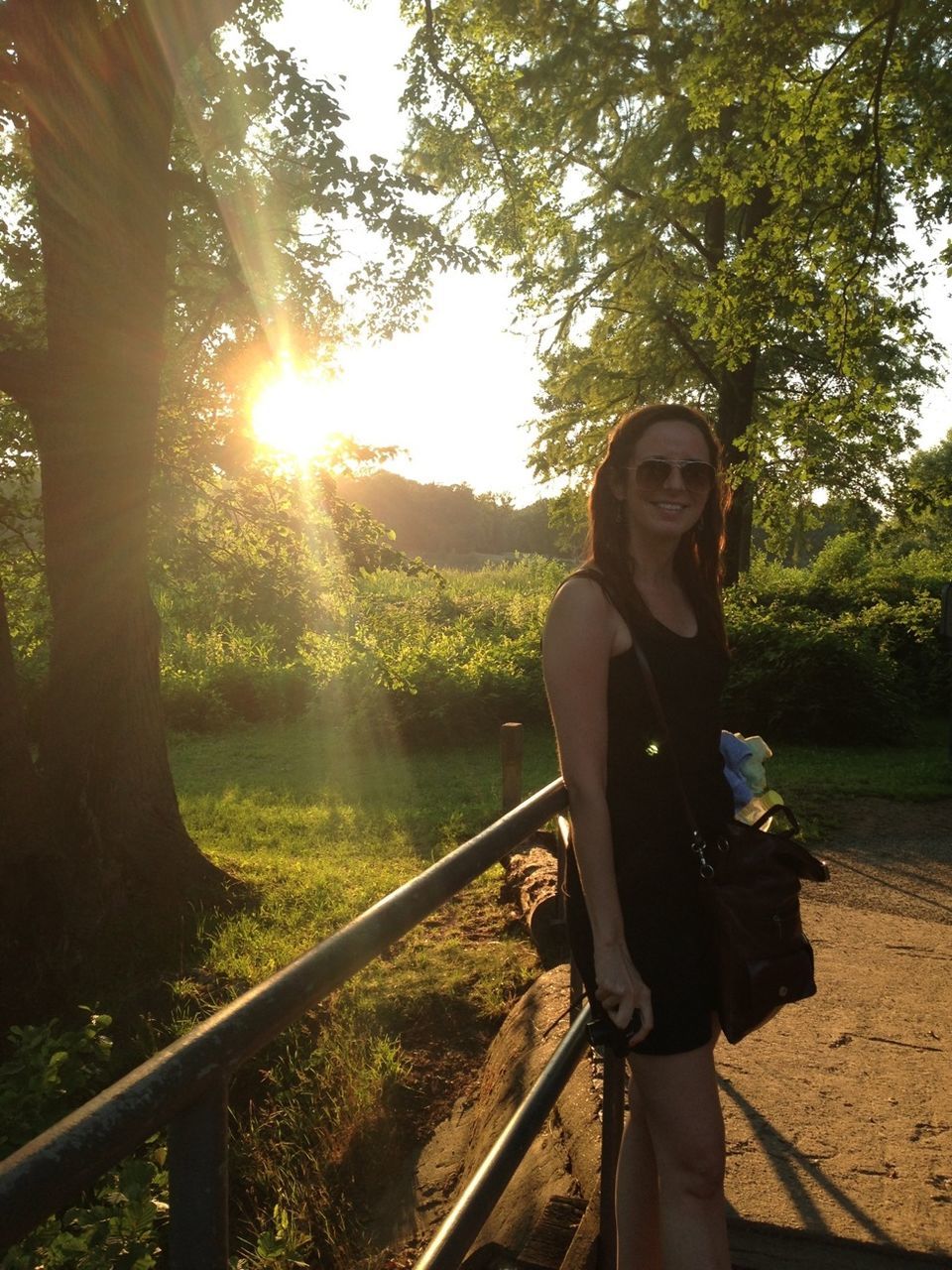 tree, lifestyles, young adult, leisure activity, casual clothing, sunlight, sun, person, standing, young women, sunbeam, railing, lens flare, three quarter length, nature, portrait, sitting, looking at camera