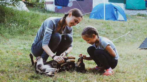 Mother and daughter playing dog on grassy land