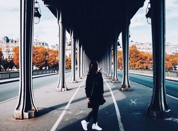 Full length of woman standing below bridge amidst streets in city during autumn