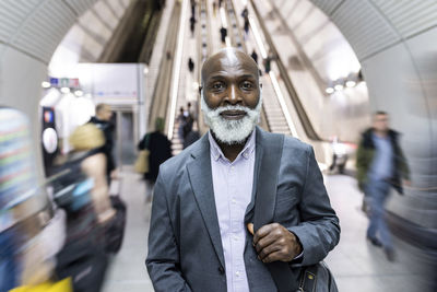 Smiling bald businessman with laptop bag amidst commuters at subway station