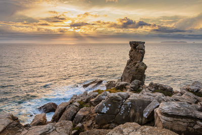 Rock on beach against sky during sunset