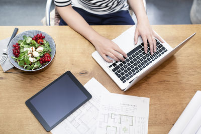 Woman at desk using laptop next to construction plan and salad