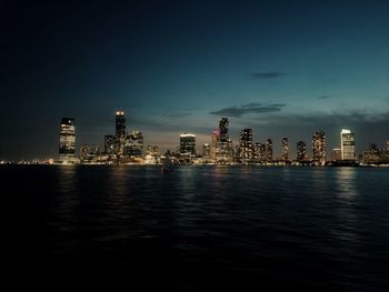 Buildings by river against sky at night