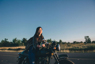 Young woman riding motorcycle on road against clear sky