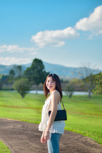 Young woman standing on field against sky