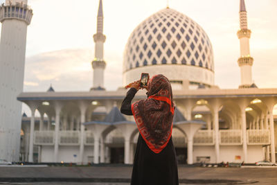 Woman photographing mosque against sky