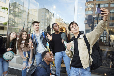 Cheerful friends taking selfie on footpath by store in city