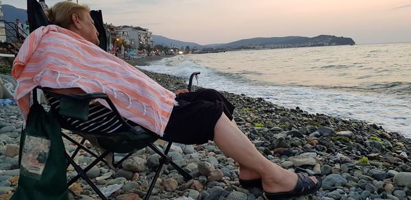 Rear view of woman on rock at beach against sky