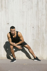 Full length of young man sitting against wall