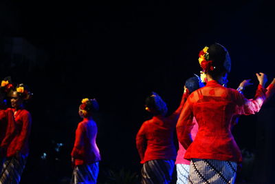 Rear view of people dancing against sky at night