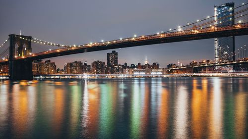 Illuminated bridge over river against sky in city at night