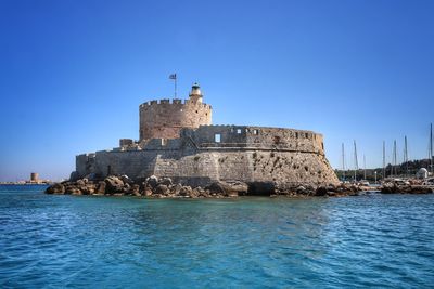 Historic building by sea against clear blue sky