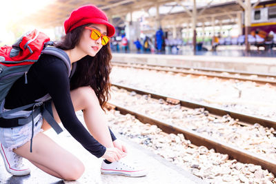 Side view of young woman with backpack tying shoelace at railroad station platform