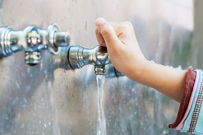 Close-up of hand holding faucet with running water