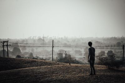 Rear view of man standing on field against sky