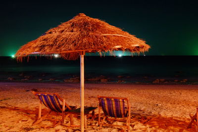 Lounge chairs on sand at beach against sky at night