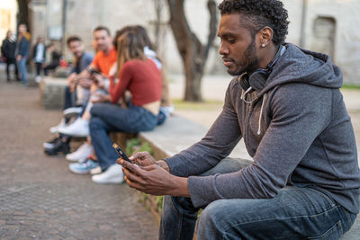 Young man using mobile phone while sitting in city