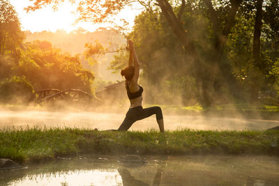 Woman doing yoga at lakeshore against trees