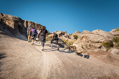 People riding motorcycle on rock formation against clear sky