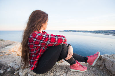 Woman sitting on rock looking at sea against sky