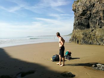 Full length of shirtless boy on beach against sky