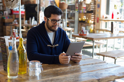 Young man reading digital tablet by bottle at table in restaurant