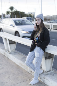 Portrait of woman talking on mobile phone while standing on road against sky