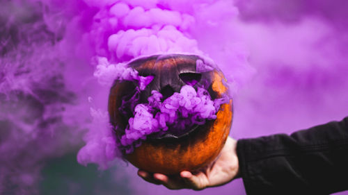 Close-up of person holding jack o lantern emitting smoke