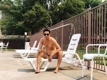 Full length of shirtless man sitting on chair