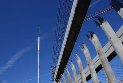 Low angle view of communications tower and security fence against clear blue sky