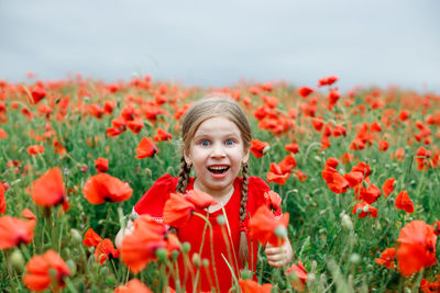 Portrait of smiling young woman with red poppy flowers in field