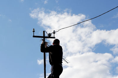 Low angle view of man standing on cable against sky