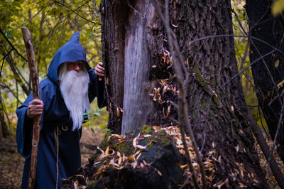 Man standing by tree trunk in forest