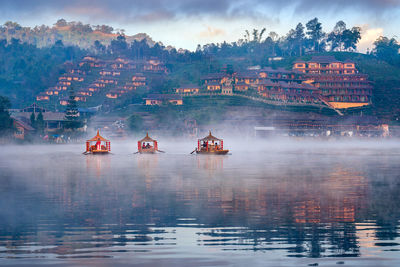 People on lake by buildings against sky