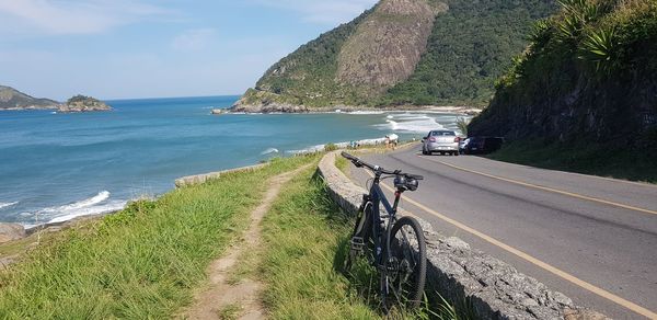 Bicycle parked on grass road by sea against sky