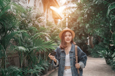 Young woman standing by plants against trees