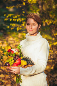 Portrait of woman holding cherry while standing by plant